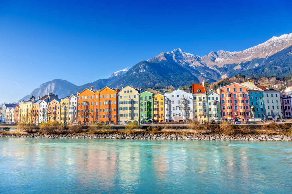 Farbenfrohe historische Häuserzeile am Ufer des Inn in Innsbruck vor der schneebedeckten Nordkette bei blauem Himmel