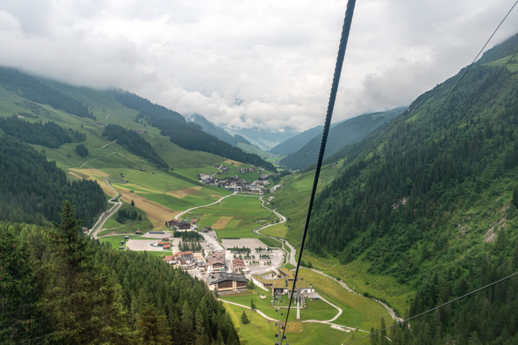 Blick von der Seilbahn auf das grüne Tuxertal mit Ortschaft, umgeben von bewaldeten Bergen und Wolken im Zillertal