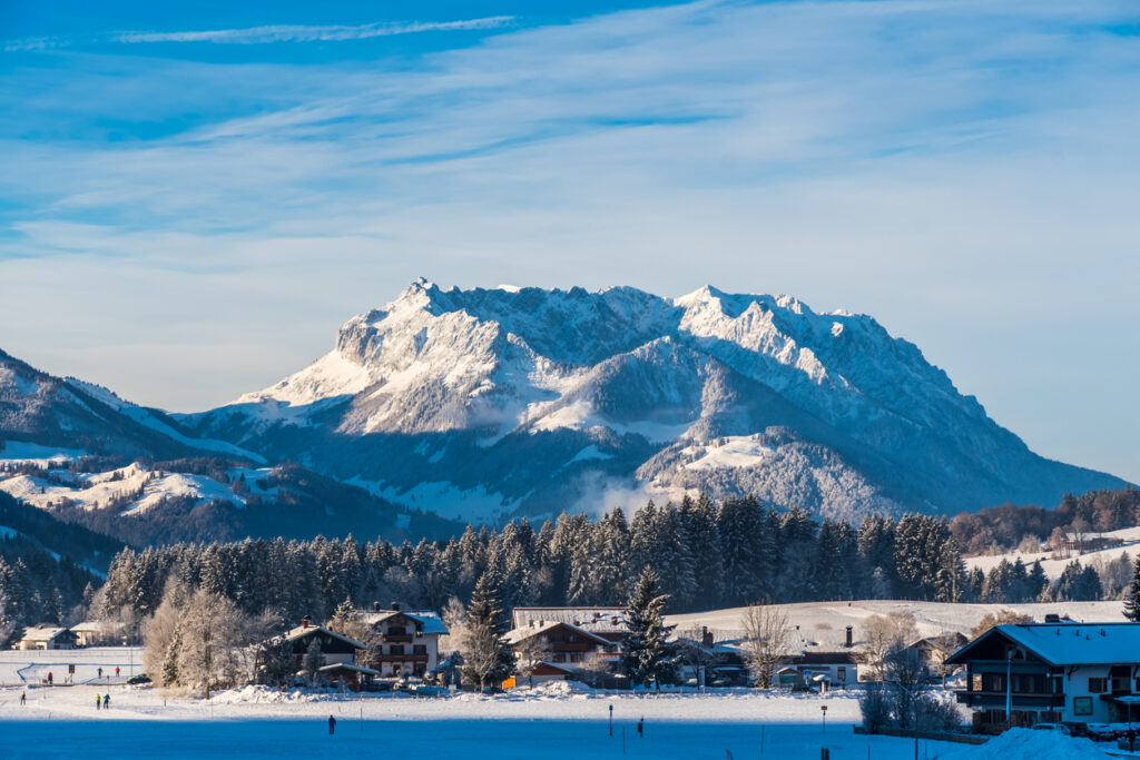 Verschneites Bergdorf in Tirol mit imposantem schneebedecktem Alpenmassiv und winterlicher Landschaft unter blauem Himmel